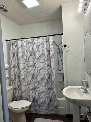 Bathroom features a shower, sink, and toilet, with a shower curtain and white tiled floor and walls.