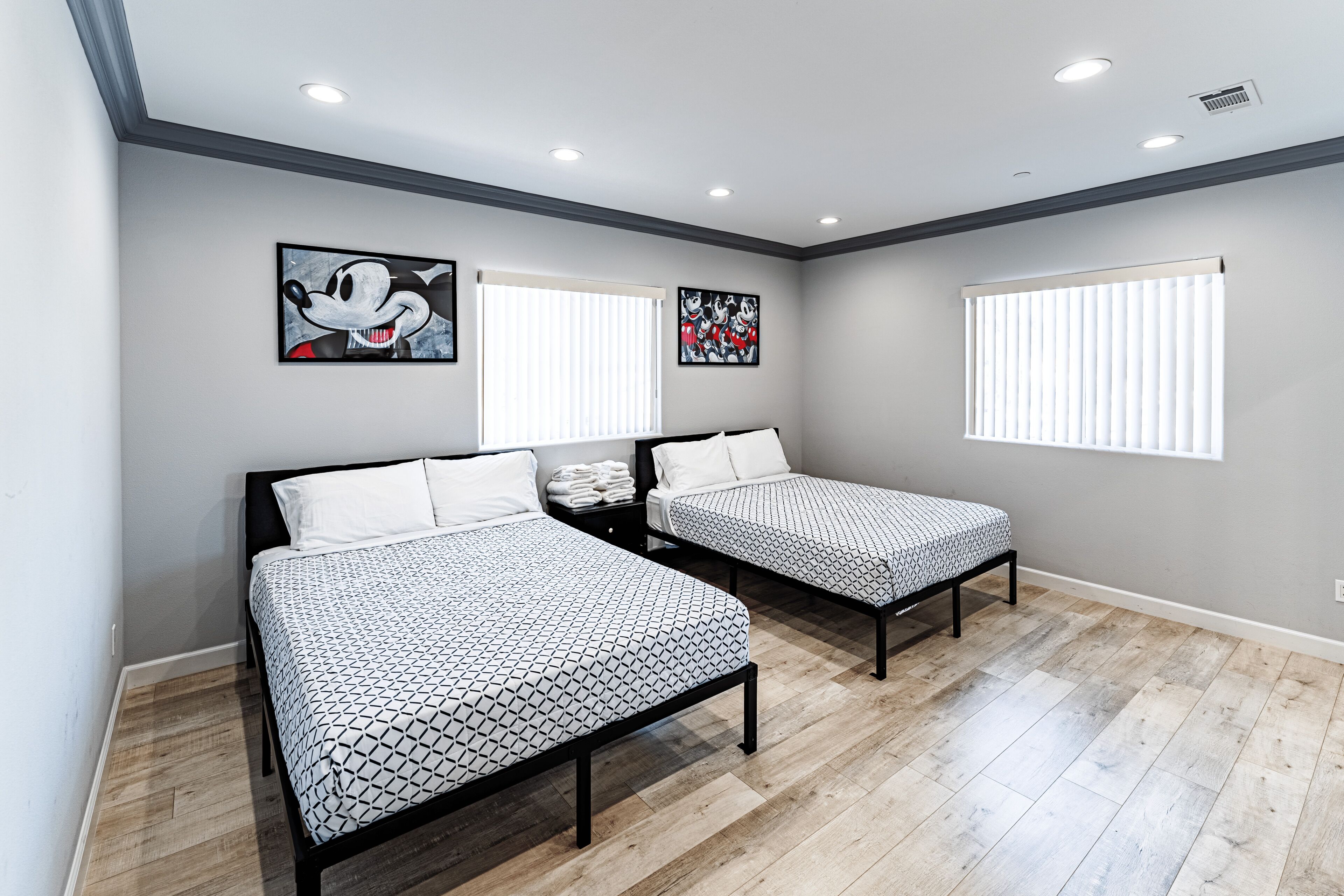 A bedroom with two beds, a nightstand, and artwork on the walls.