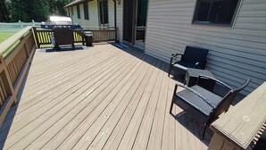 Una terraza de madera con mobiliario exterior, una parrilla y un área cubierta con un portón corredera.