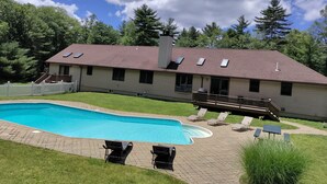 Una casa de dos pisos con piscina, un porche cubierto con sillones de descanso y un patio cercado.