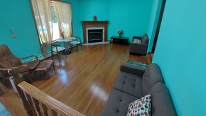 Una sala de estar con paredes color turquesa, piso de madera, chimenea, sofá, mesa de comedor con sillas y ventilador de techo.