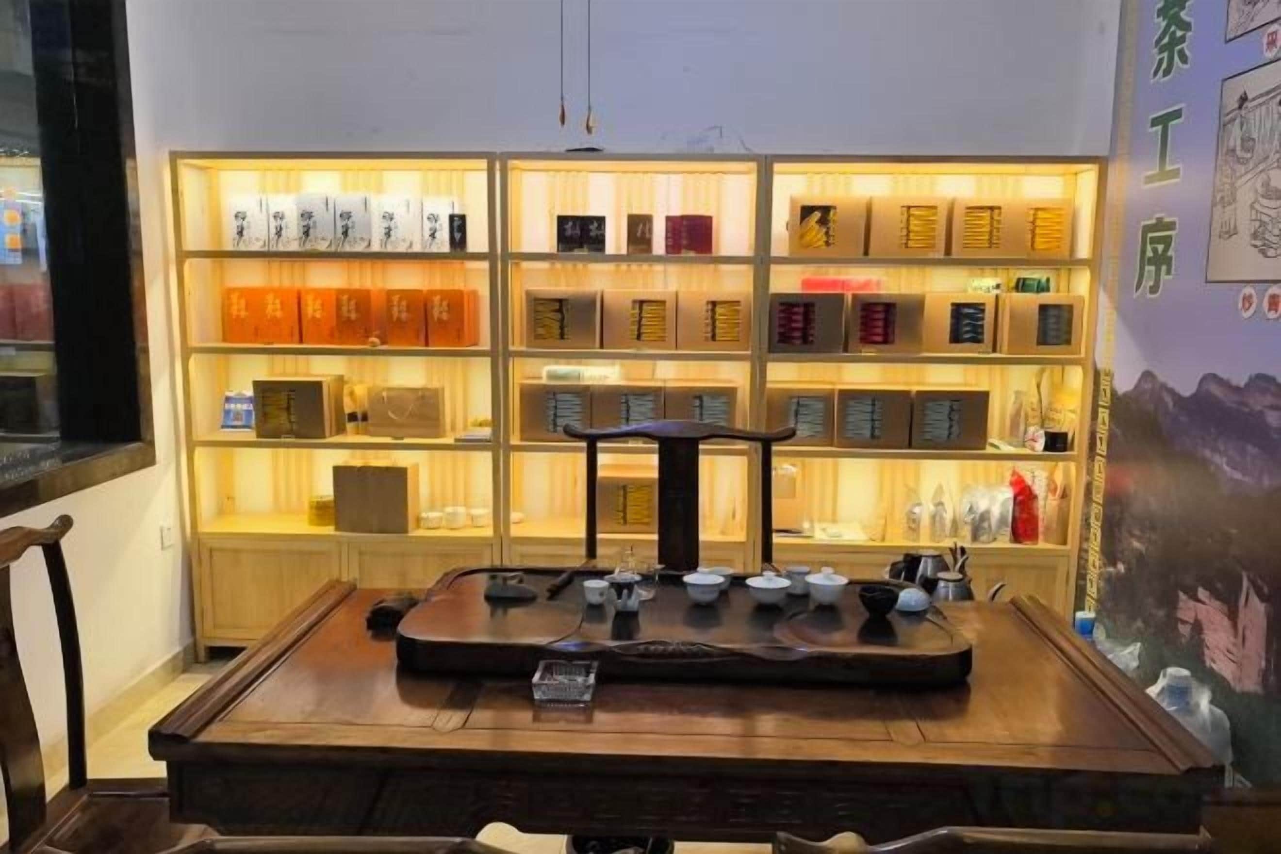 A wooden table with a tea set in front of a shelf with various items.