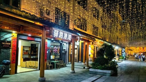 A street with illuminated string lights and a restaurant with a sign in a foreign language. - Yilu Gangwan Inn (Wuyishan)