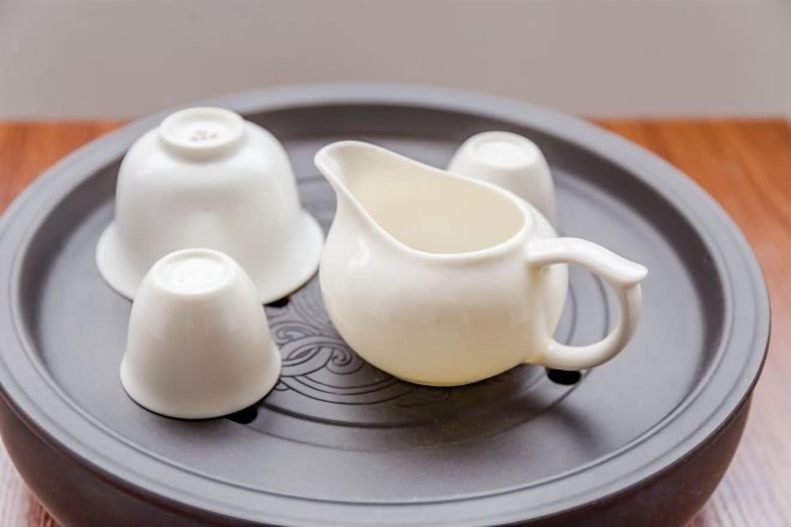 Un set di utensili da tè in ceramica bianca su un vassoio rotondo scuro.