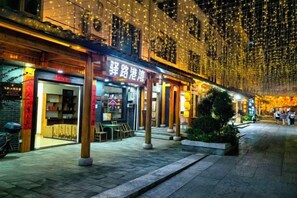 A street with shops and outdoor seating, illuminated by string lights. - Yilu Gangwan Inn (Wuyishan)