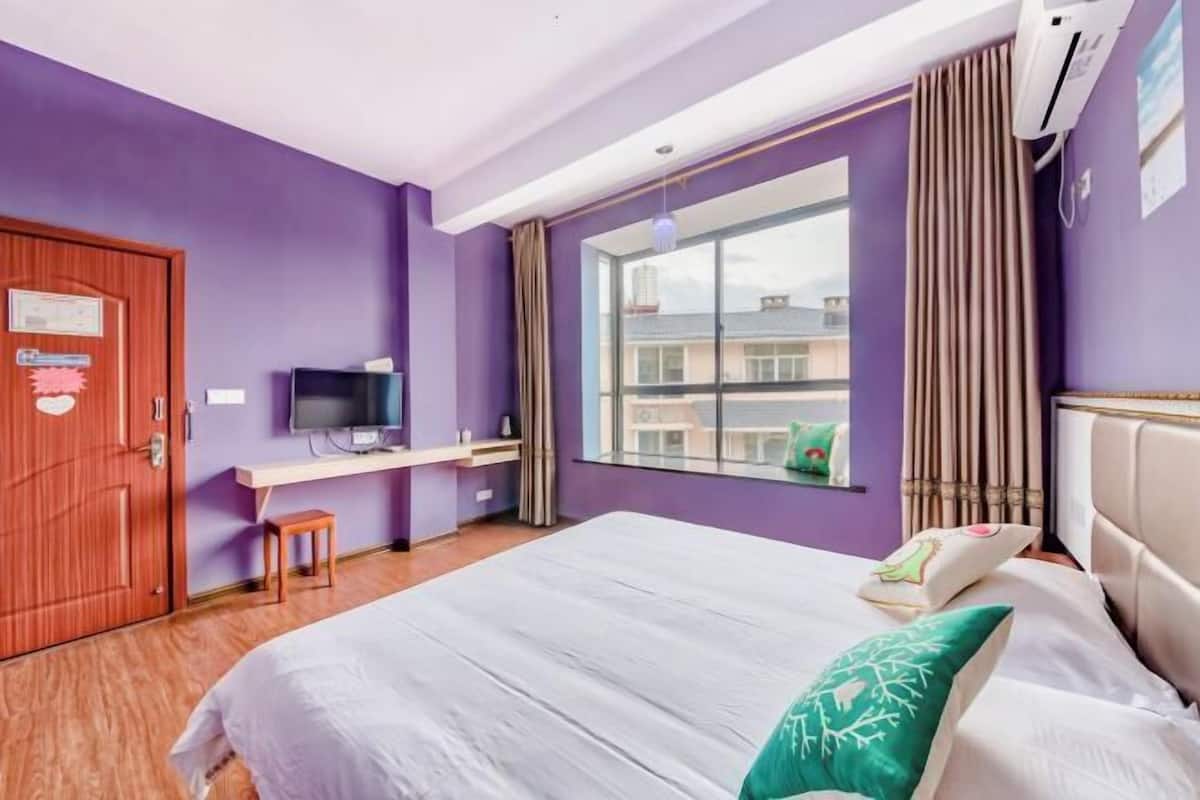 A bedroom with a bed, a desk, a television, and a window with curtains.
