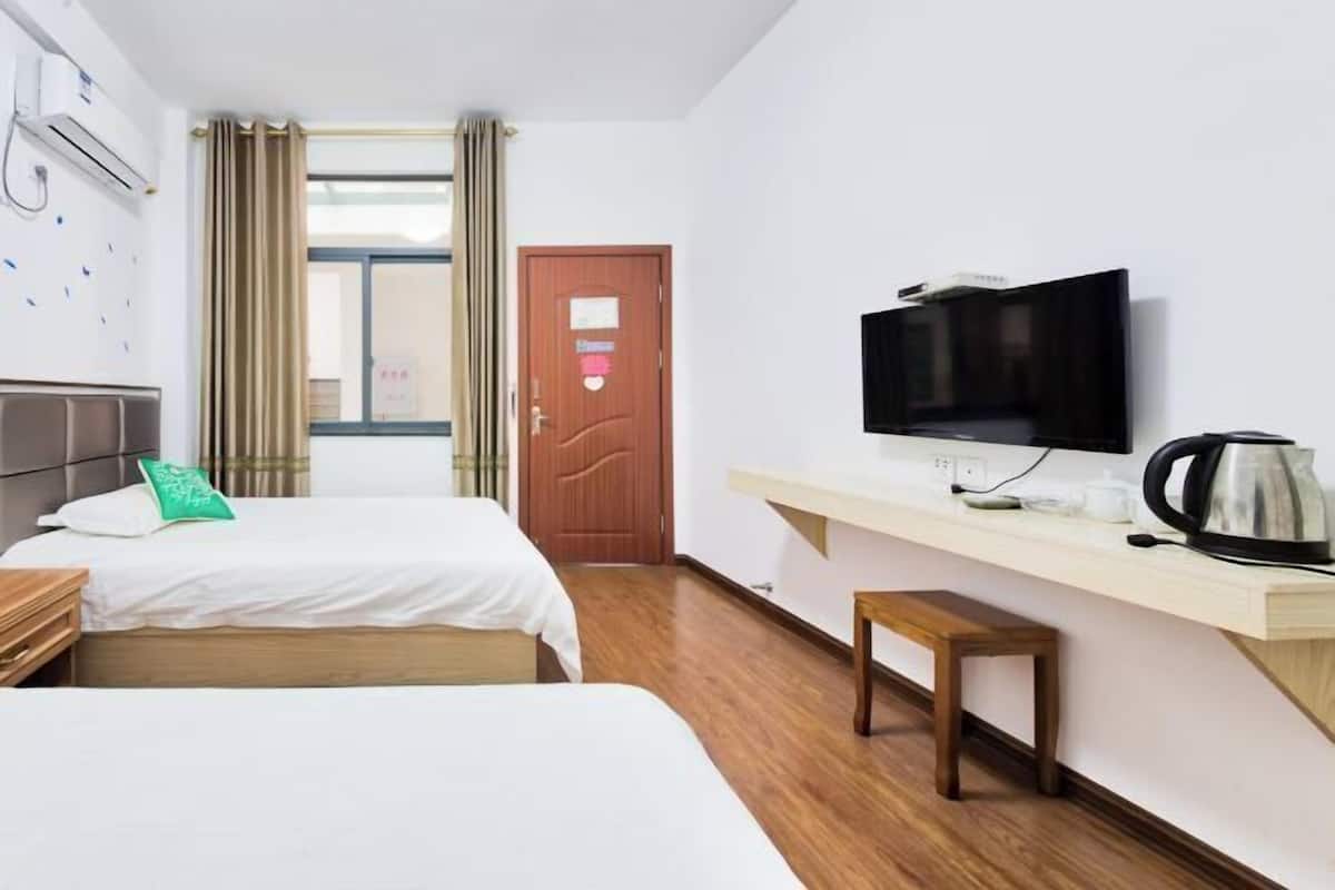 A hotel room with two beds, a TV, a coffee maker, and a wooden bench.