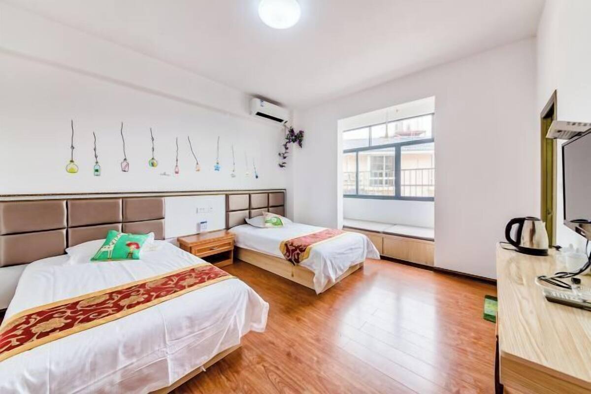 A hotel room with two beds, a wooden floor, a window with a view, and a desk with a kettle.