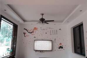 A room with a ceiling fan, a flat-screen TV, and decorative wall art. - Yilu Gangwan Inn (Wuyishan)