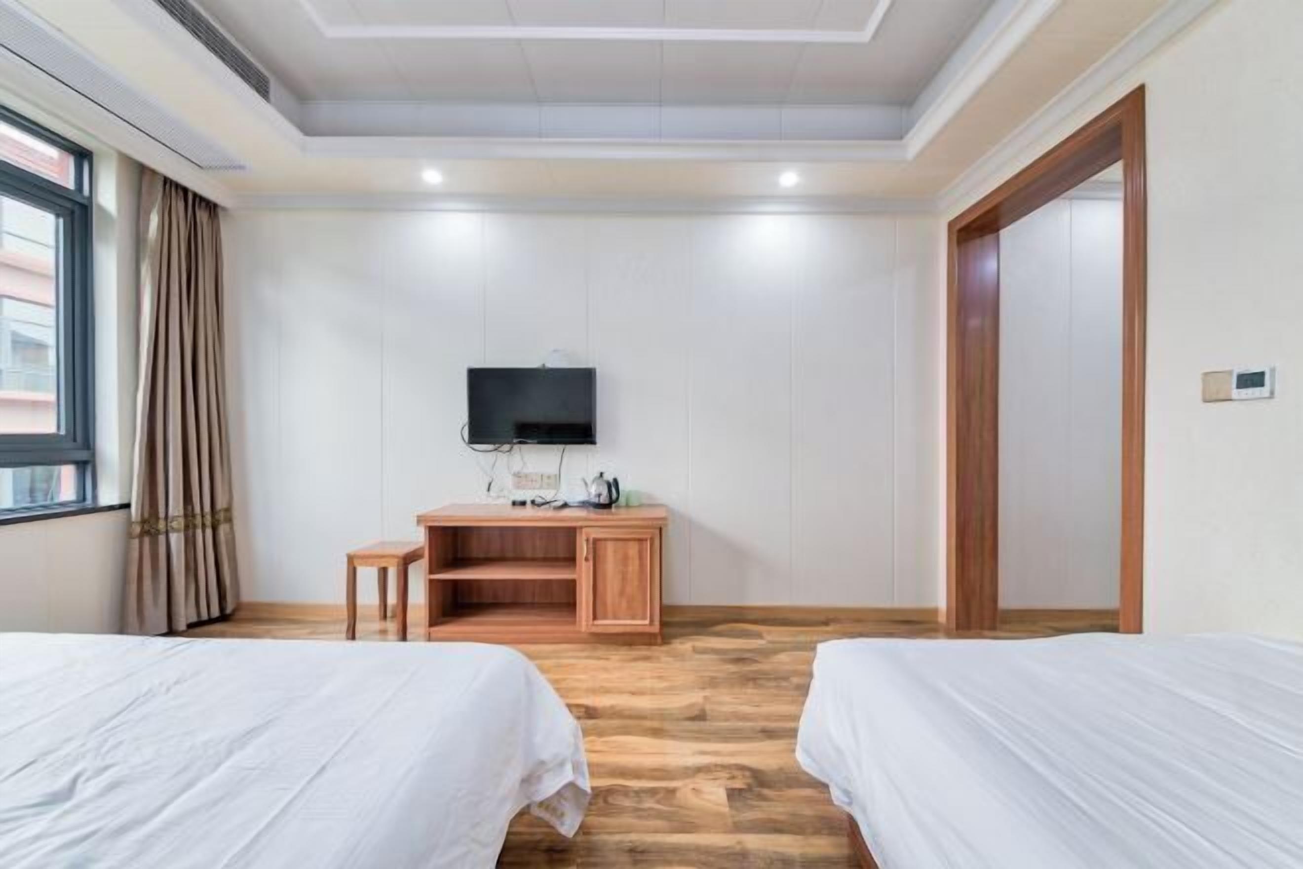 Une chambre d’hôtel avec deux lits, un bureau en bois, une télévision et une armoire.