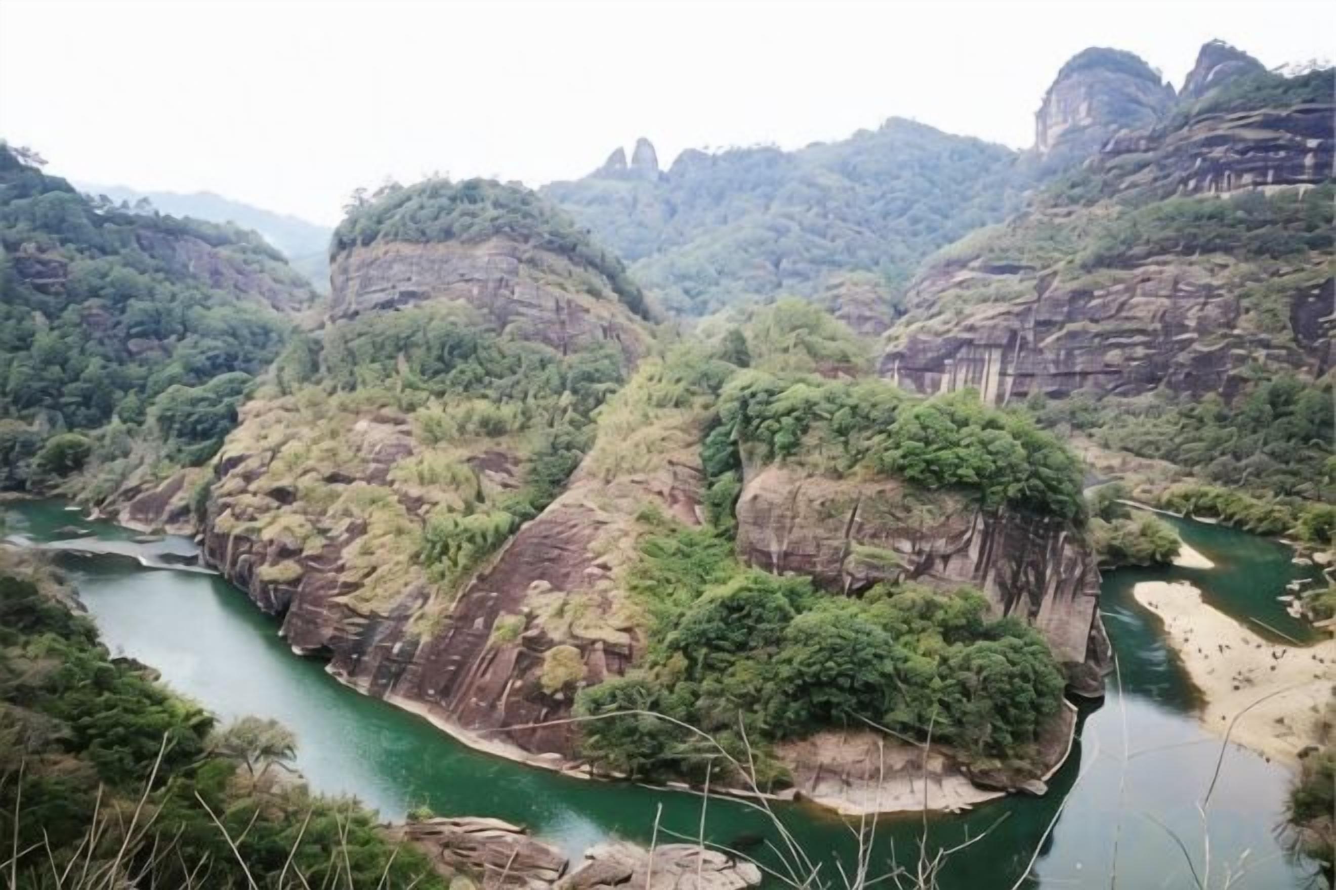 Un fiume serpeggia attraverso un paesaggio montuoso con scogliere rocciose e vegetazione fitta.