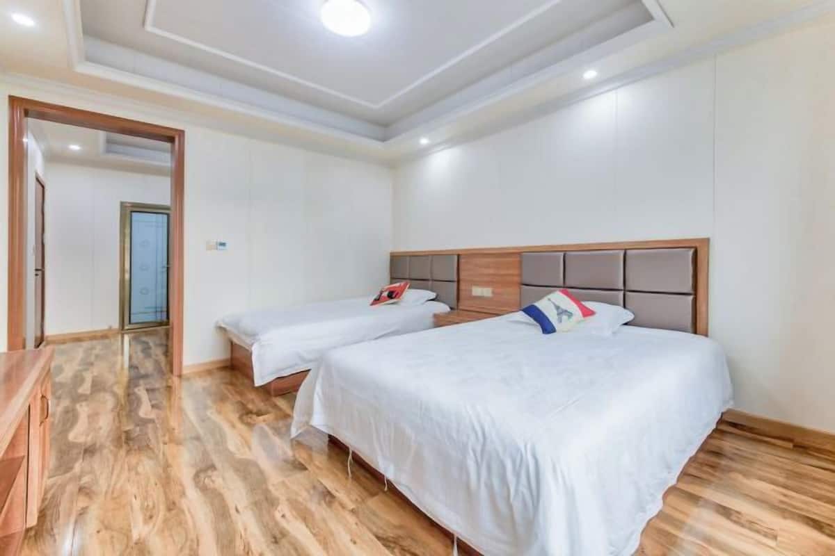 A hotel room with two beds, wooden flooring, and a ceiling with recessed lighting.