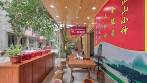 A restaurant interior with a wooden reception desk, wooden stools, and a mural on the wall. - Yilu Gangwan Inn (Wuyishan)