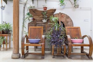A room with two wooden chairs, a wooden table, and a rustic fireplace with plants. - Yilu Gangwan Inn (Wuyishan)