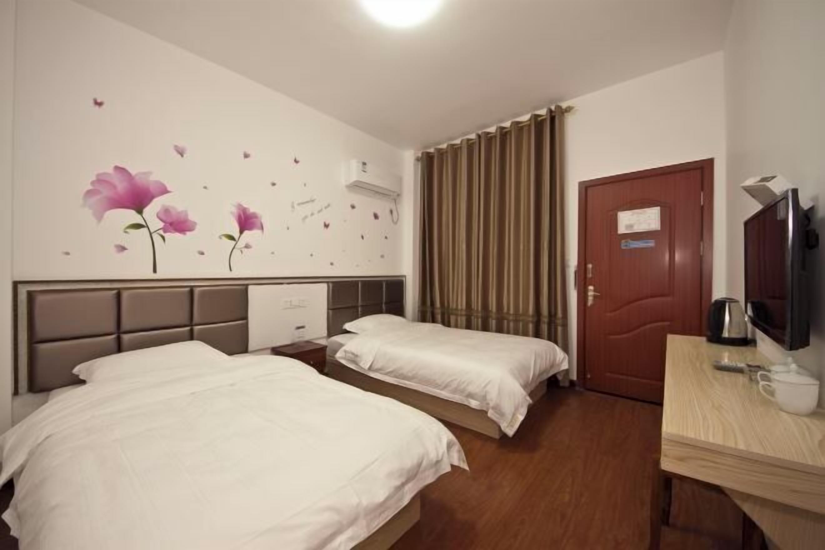 Une chambre d’hôtel avec deux lits, un bureau en bois, une télévision et une porte avec une pancarte.