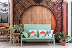 A green bench with decorative pillows, a wooden wall with a geometric pattern, and potted plants.