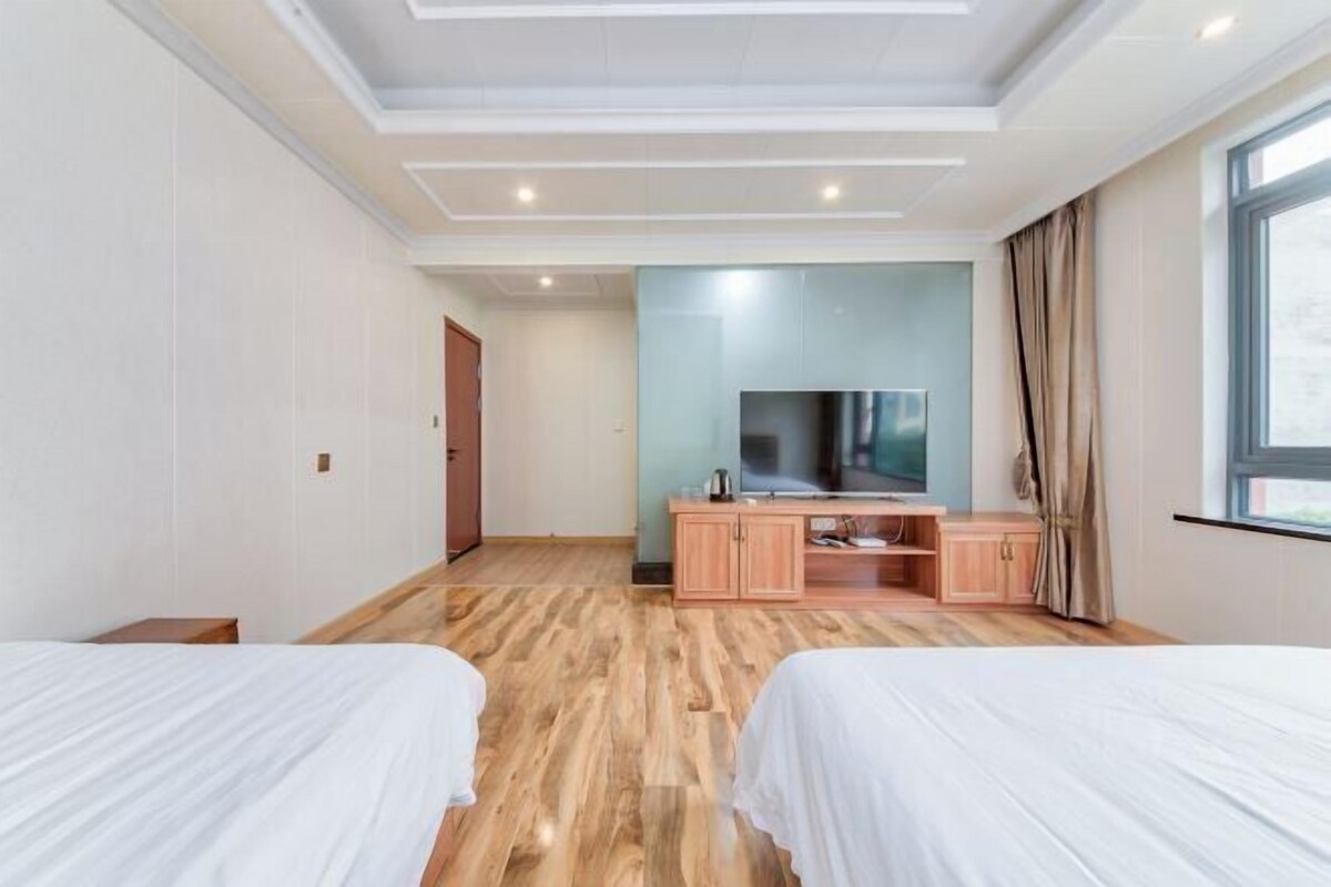 A hotel room with two beds, a TV, a wooden cabinet, and a large window.