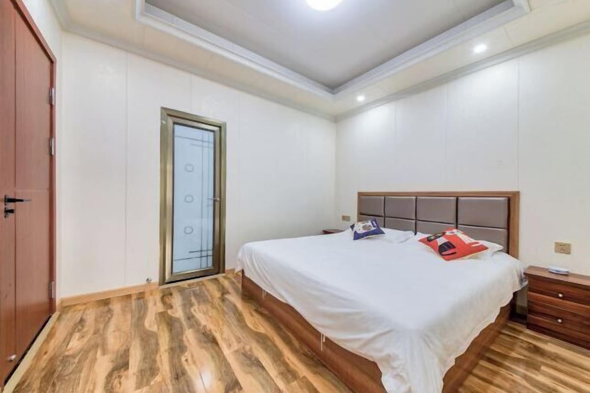 A bedroom with a wooden floor, a bed with a white bedspread, a nightstand, and a wooden wardrobe.