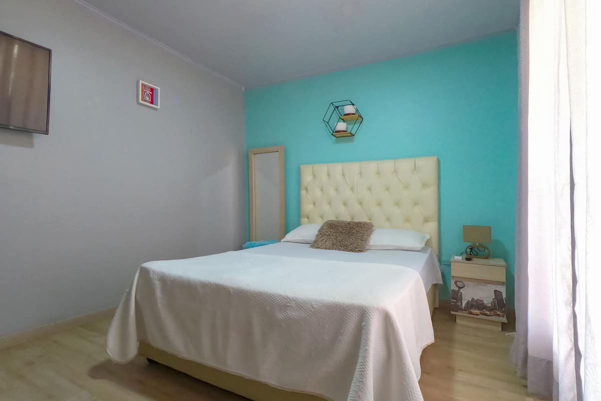 A bedroom with a bed, a nightstand, a mirror, and a wall-mounted lamp.