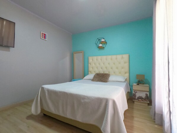 A bedroom with a bed, a nightstand, a mirror, and a wall-mounted lamp.