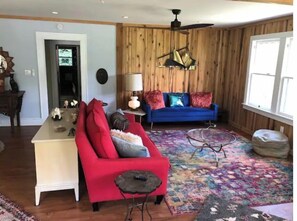 Un salon avec un canapé rouge, une petite table blanche, un divan bleu, un mur en bois et un ventilateur de plafond.