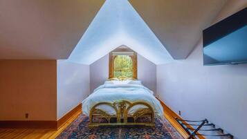 A bedroom with a sloped ceiling, a bed with ornate headboard, a large window, and a TV mounted on the wall.