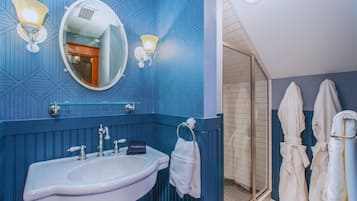 Une salle de bain équipée d’un lavabo, d’un miroir et de deux appliques murales. On y trouve des serviettes et un porte-peignoir avec des peignoirs.