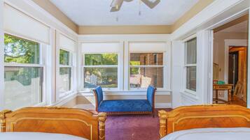 A room with two wooden beds, a blue bench, large windows, and a view of greenery outside.
