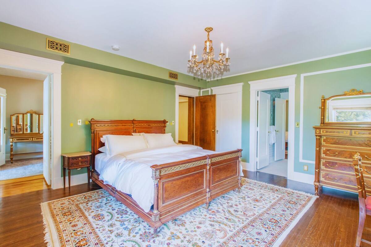 A spacious bedroom with a large bed, a chandelier, and a wooden dresser.
