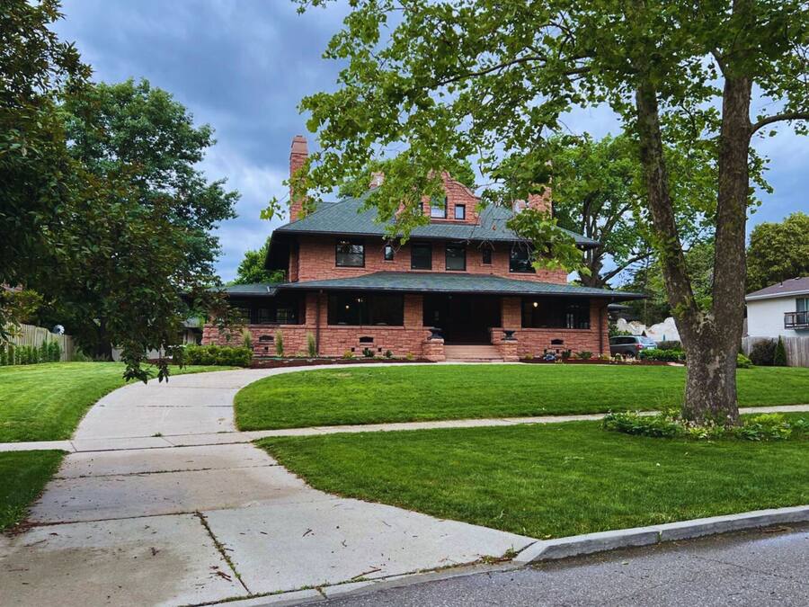 A two-story brick house with a front porch, a chimney, and a well-maintained lawn.