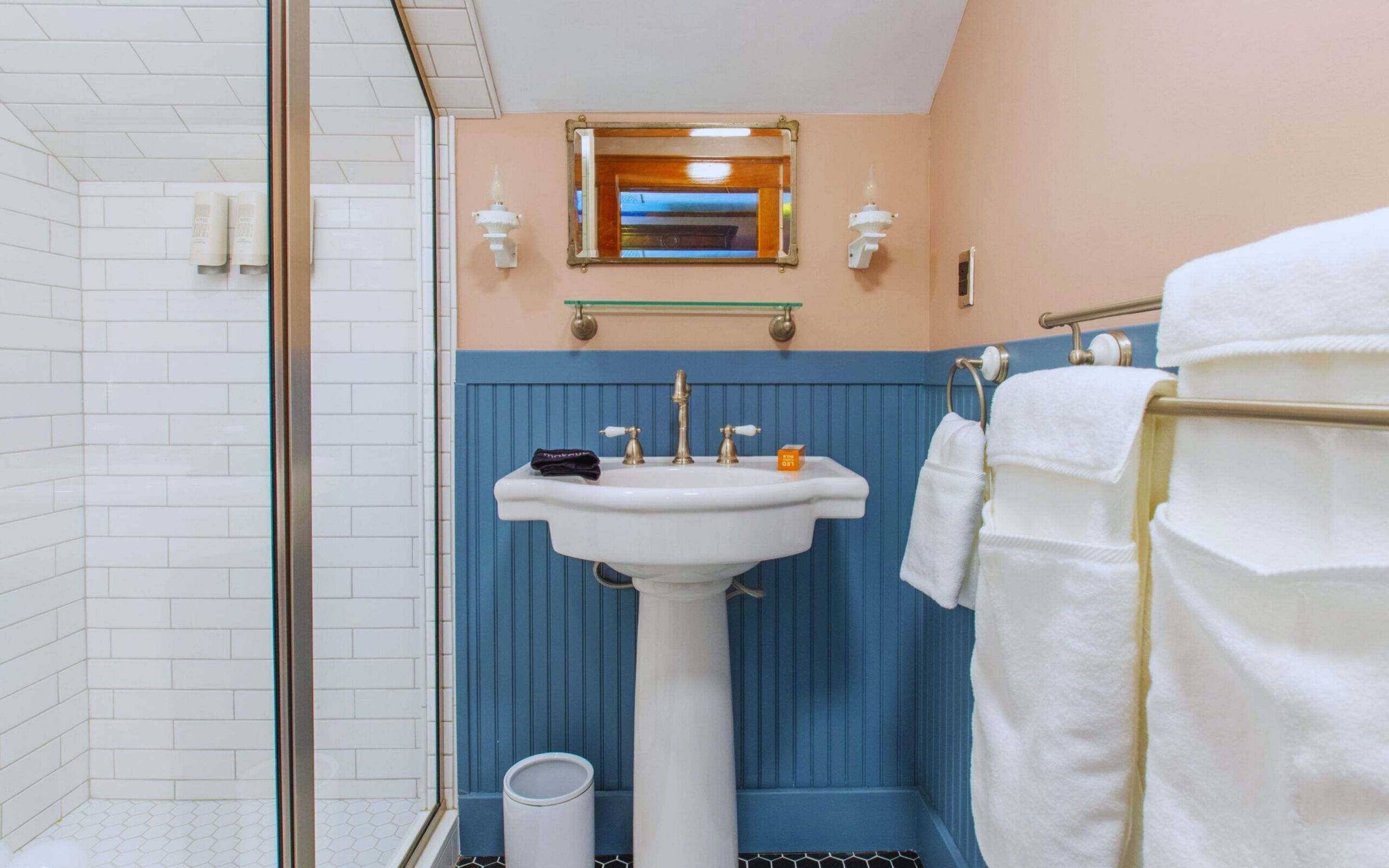 A bathroom with a white sink, blue wall paneling, a mirror, and a towel rack with white towels.