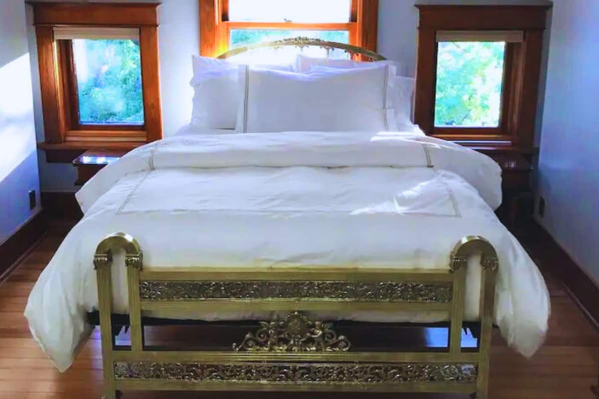 A bedroom with a large bed, two windows with wooden frames, and a sloped ceiling.