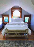 Un dormitorio con una cama grande, dos ventanas con marcos de madera y un techo inclinado.