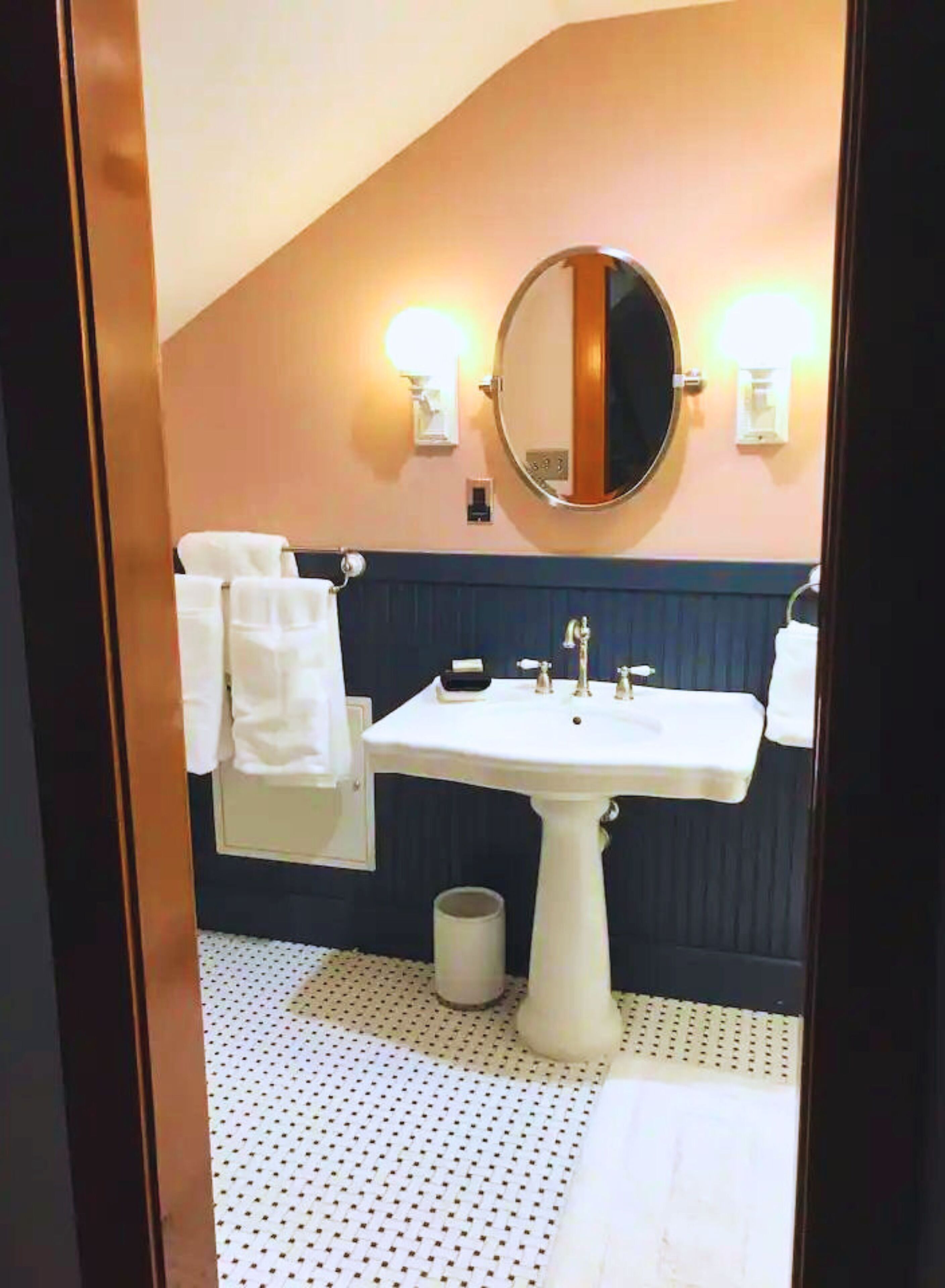 Een badkamer met een witte wastafel, een ronde spiegel en twee wandlampen.