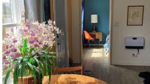 A dining area with a round wooden table, a wicker plant, and a view into a room with a desk and chair. - Not available (Sylva)