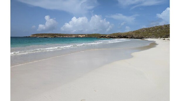 A wide sandy beach with gentle waves, a clear sky, and a distant rocky outcrop. - Cheerful Home with Gorgeous Ocean Views and Pool (Vieques,)