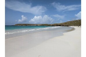 Ein weiter Sandstrand mit sanften Wellen, einem klaren Himmel und einer in der Ferne liegenden Felsformation.
