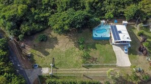 An aerial view of a property with a swimming pool, a covered area with solar panels, and a fenced yard.
