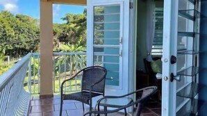 A balcony with two chairs and a table, a ceiling fan, and a view of greenery. - Cheerful Home with Gorgeous Ocean Views and Pool (Vieques,)