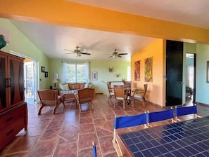 A spacious dining area with a high ceiling and two ceiling fans, a dining table with chairs, and a view of the outside through a window with blinds.