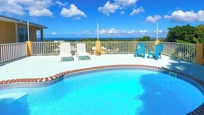 A pool area with a view of the ocean, surrounded by a white fence and blue chairs. - Cheerful Home with Gorgeous Ocean Views and Pool (Vieques,)