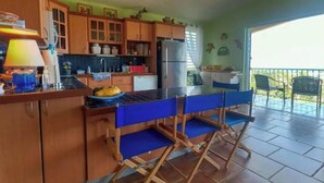 A kitchen with wooden cabinets, a refrigerator, and a dining area with blue chairs. - Cheerful Home with Gorgeous Ocean Views and Pool (Vieques,)