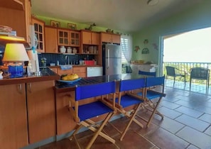 A kitchen with wooden cabinets, a refrigerator, and a dining area with blue chairs.