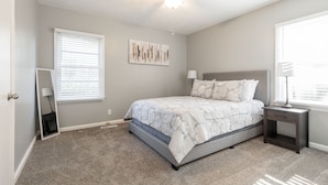 A bedroom with a bed, a ceiling fan, a bedside table, and a window with blinds.