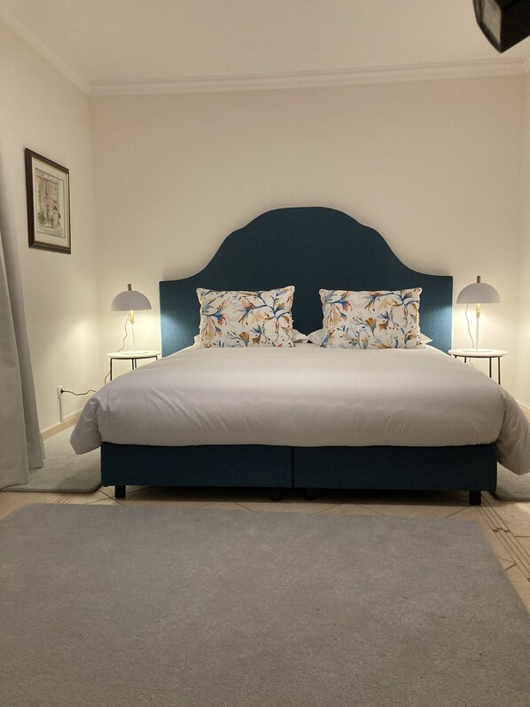 A neatly made bed with a dark headboard, two matching lamps on either side, and a framed picture on the wall.