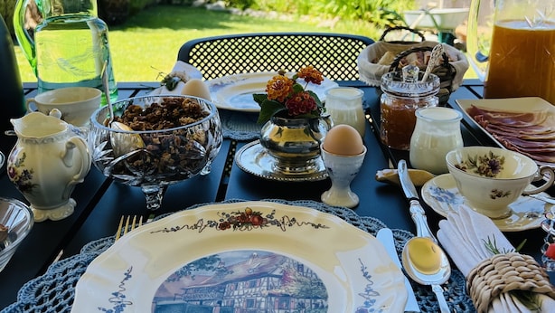A table set outdoors with a variety of dishes, including a pitcher, a bowl of nuts, a cup of coffee, and a plate with a floral design. - Villa Tranberg (Silves)