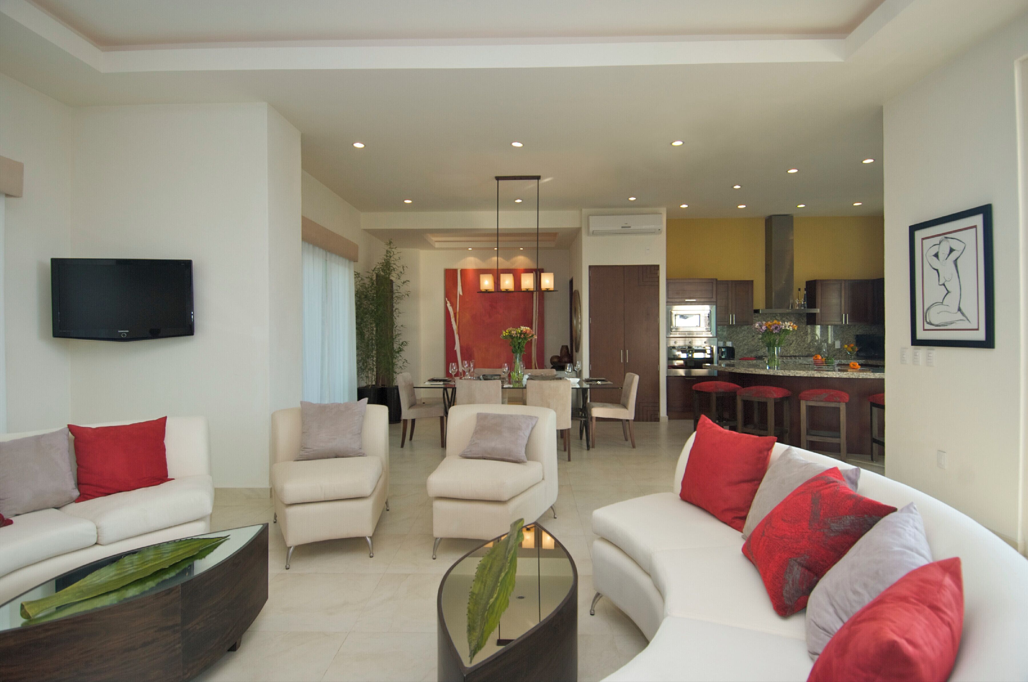 A modern living room with a sofa, armchairs, and a coffee table. There is a dining area with a table and chairs, and a kitchen with a bar area.