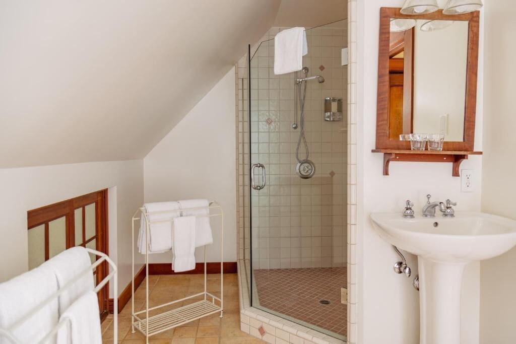 Un baño con ducha de vidrio, lavamanos blanco y espejo con marco de madera.