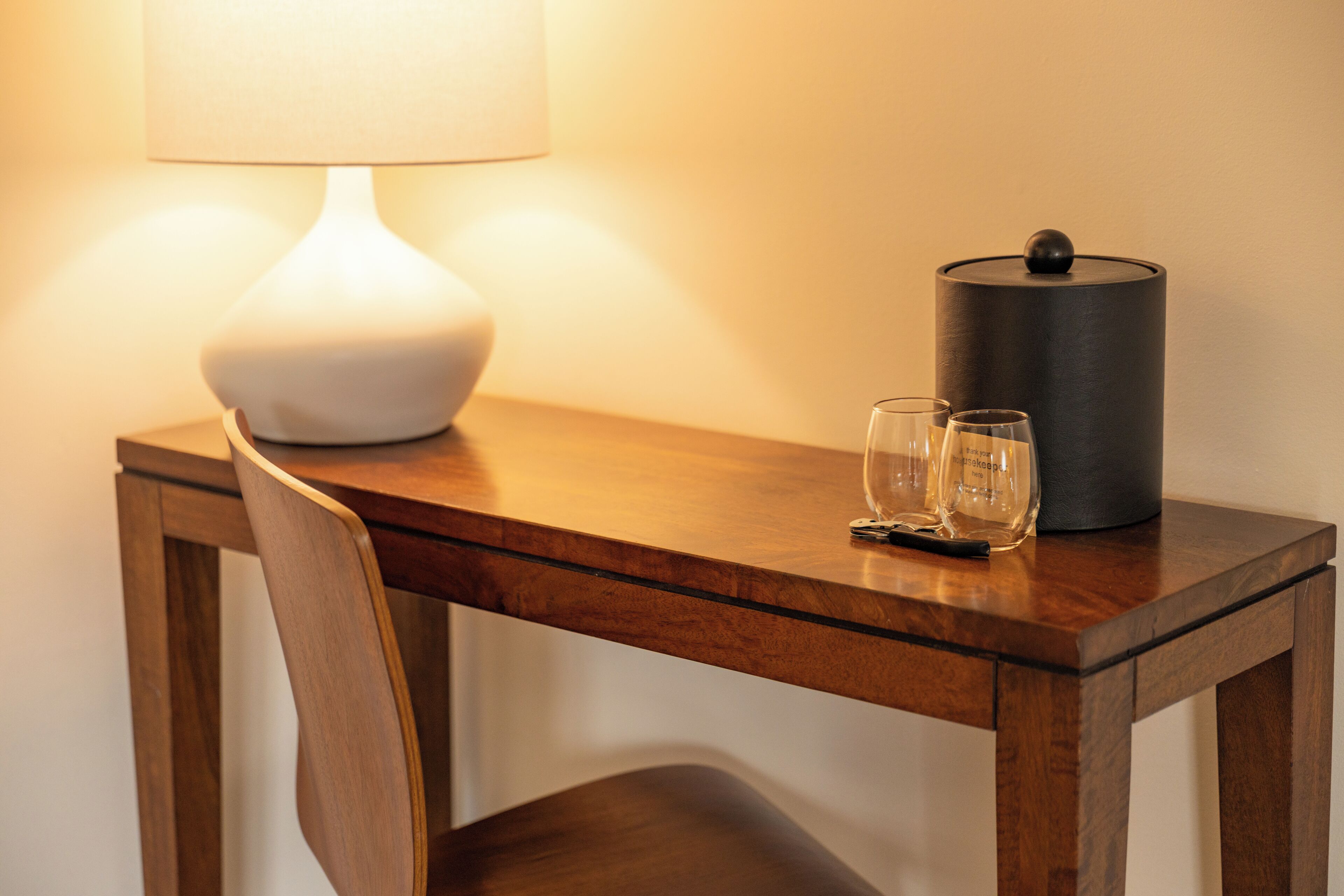 Ein Holztisch mit einer Lampe, zwei Gläsern und einem schwarzen Behälter.