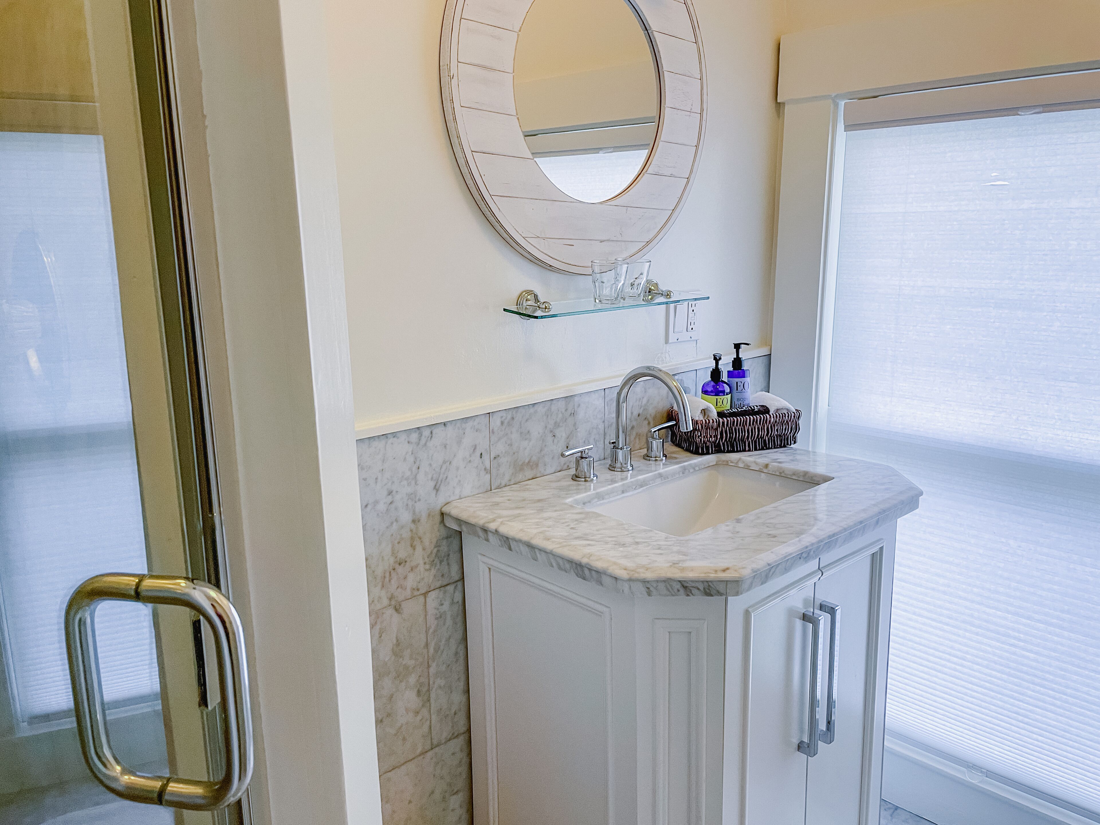 A bathroom with a marble sink, a glass shelf with toiletries, and a large mirror.